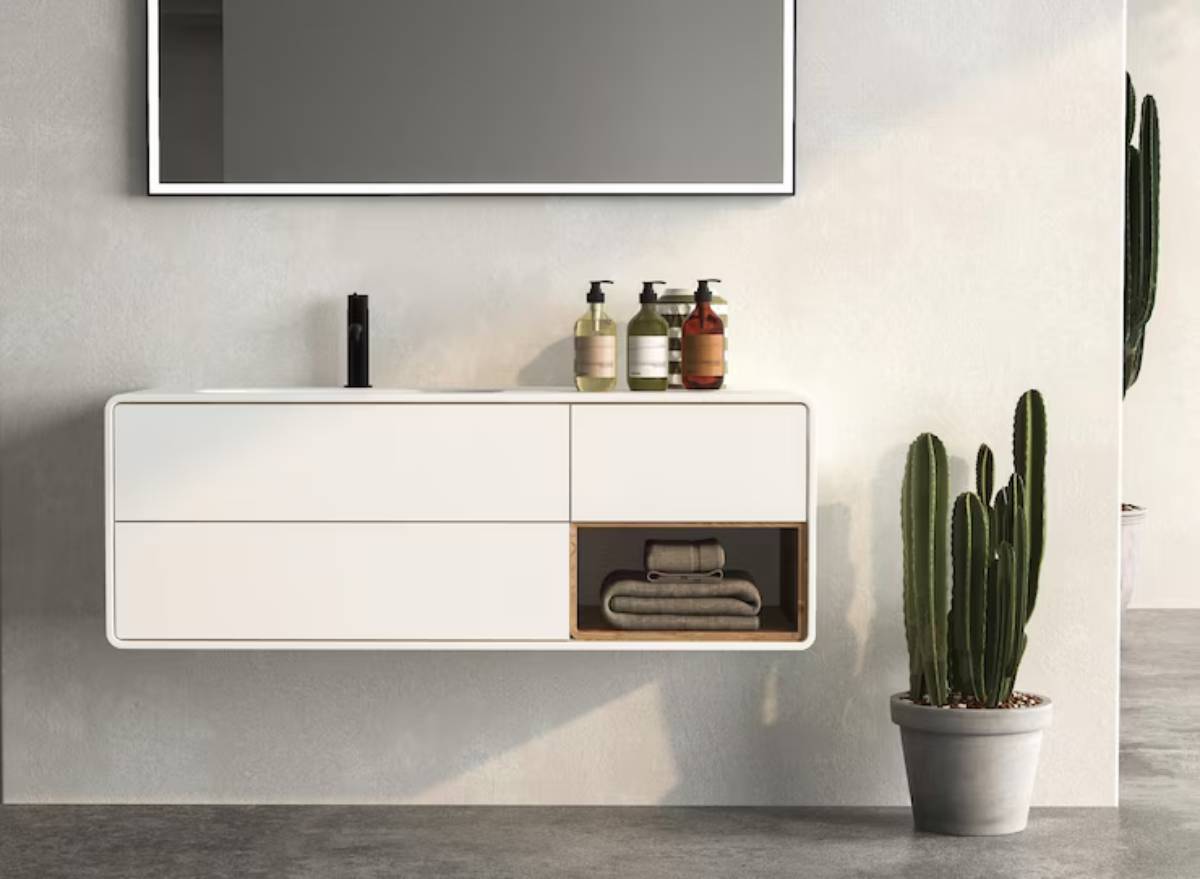 Modern bathroom setup featuring a sleek white cabinet with towels, soap bottles, and a tall cactus in a pot against a concrete wall.