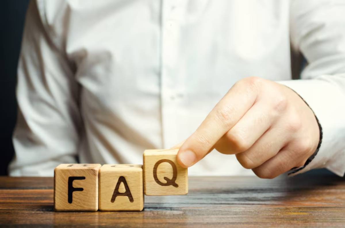 A person's hand places a wooden block labeled Q next to F and A on a table, creating the acronym FAQ.