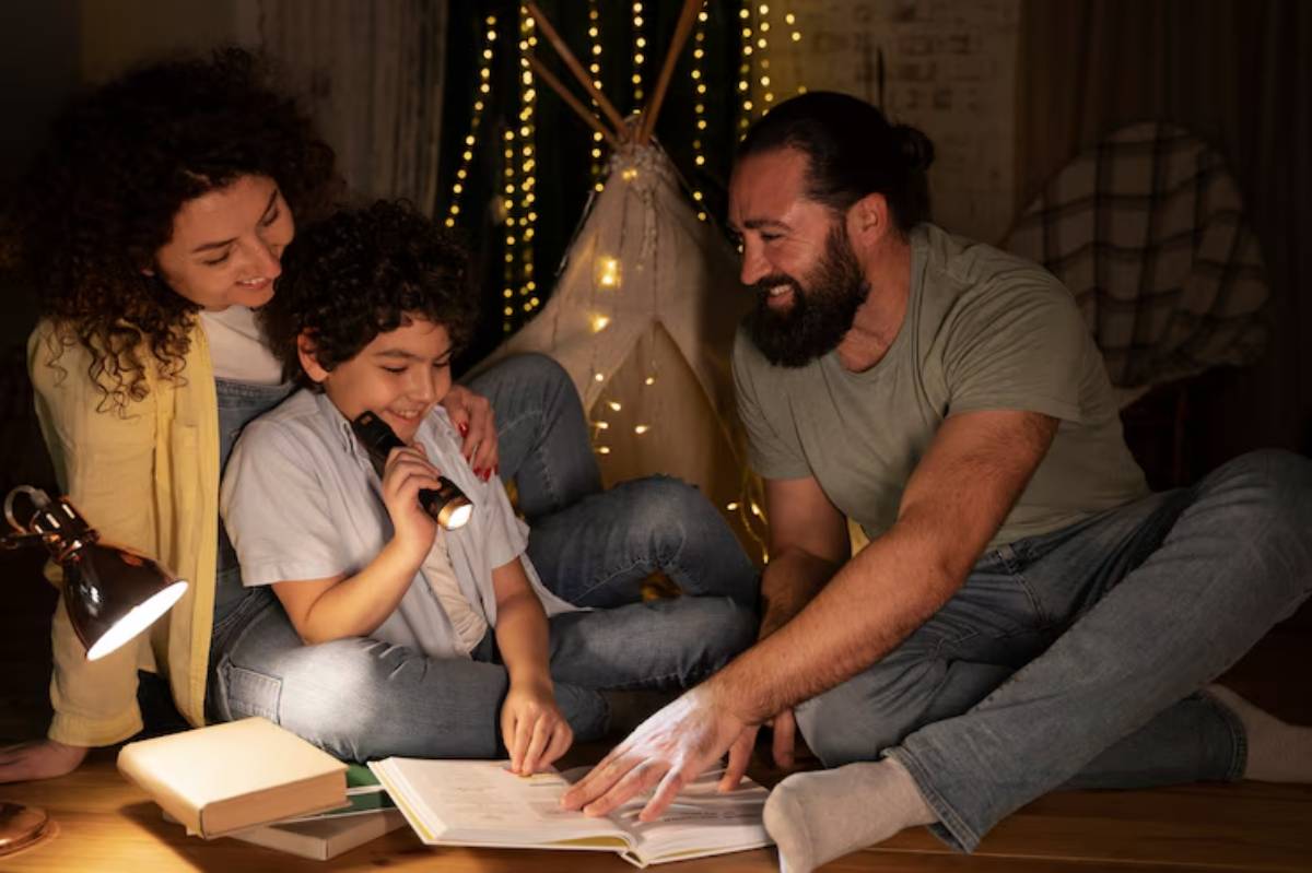 A family enjoys storytime together in a cozy, dimly lit room, illuminated by fairy lights, with a book and a flashlight in hand.