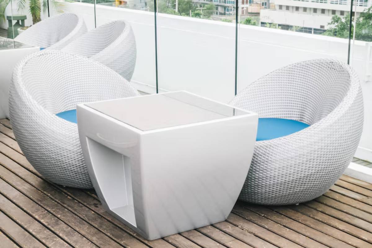 Two stylish white woven chairs with blue cushions beside a modern white table on a wooden deck, overlooking a city view.
