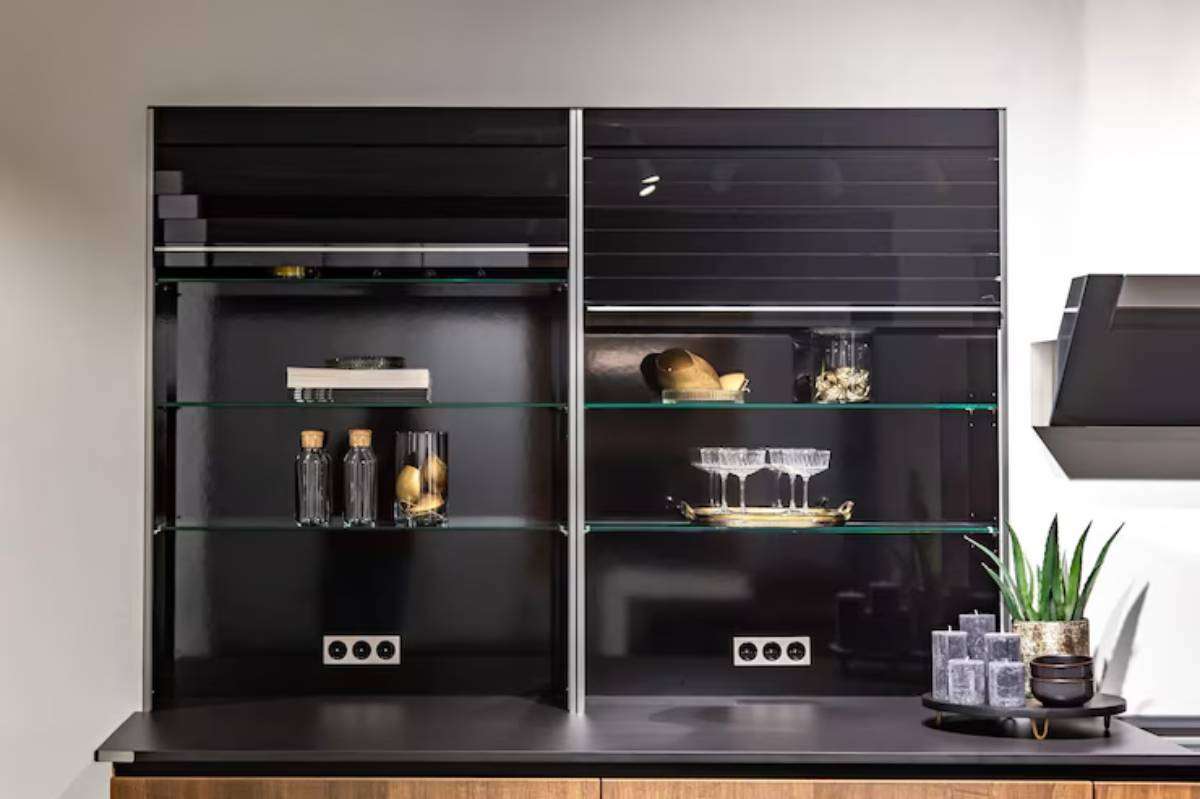 Modern black wall cabinet with glass shelves displaying decorative items, bottles, and candles, alongside an elegant countertop.