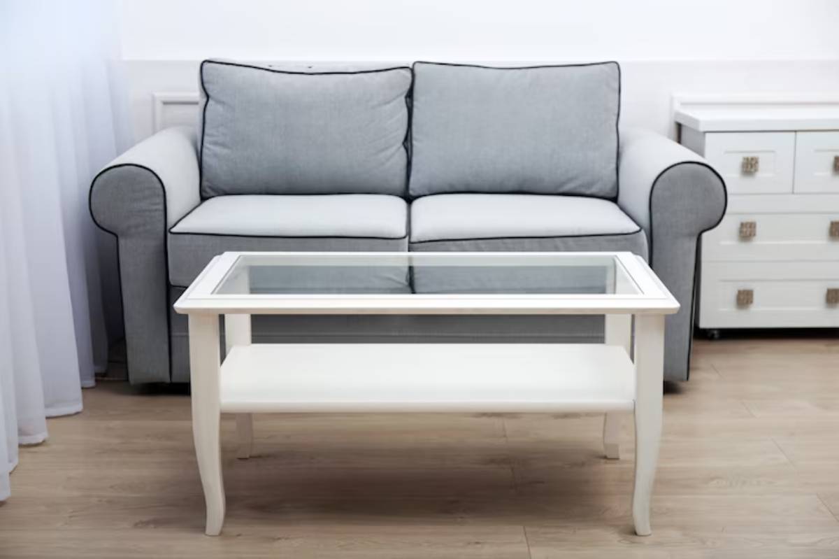 A cozy living room featuring a gray couch with cushions, a white coffee table with a glass top, and a light wooden floor.