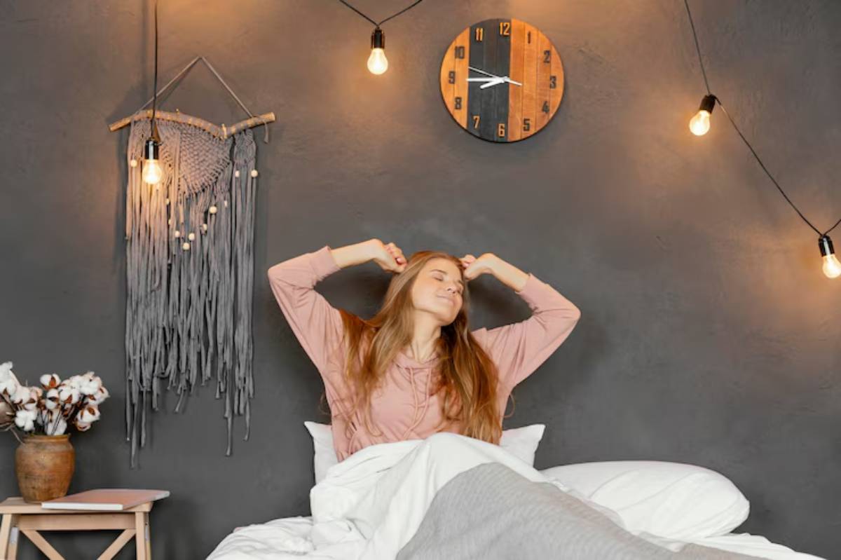 A cozy bedroom scene features a person stretching in bed, surrounded by soft pillows and warm lighting, creating a relaxed atmosphere.