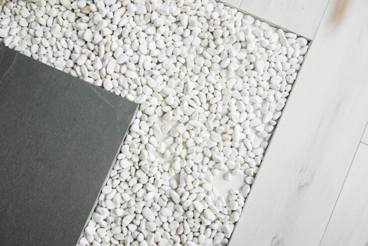 A close-up of white pebbles beside a dark slate tile, contrasting textures against a light wooden floor.