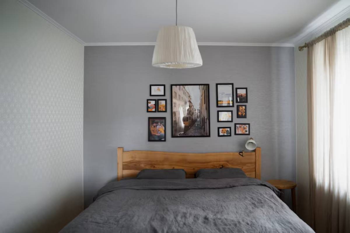 Cozy bedroom featuring a wooden bed with gray linens, framed photos on the wall, a bedside lamp, and soft curtains.
