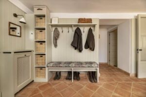 Cozy entrance hall featuring a bench, hooks for coats, storage baskets, and rustic tile flooring for a welcoming atmosphere.