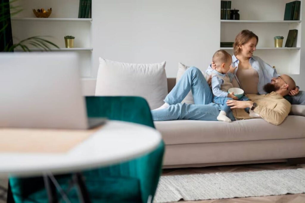 A cozy family scene on a beige sofa, with a child and adult sharing a bowl, surrounded by a modern, minimalistic living space.