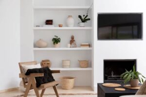 A cozy living space featuring a wooden chair, minimalist shelves with decor, and a TV above a sleek fireplace.