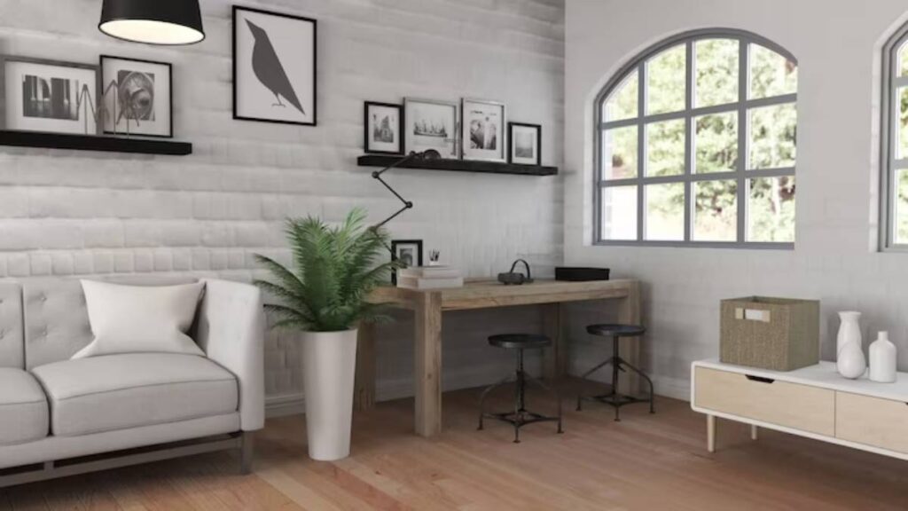 Modern living room with a white couch, wooden desk, green plant, black and white artwork, and large windows letting in natural light.